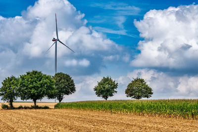 Wind turbine on land against cloudy sky