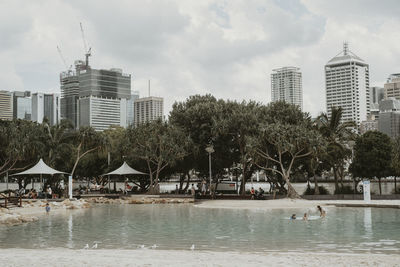 Buildings by river against sky in city
