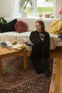 Delighted female radio host recording podcast while using mic and reading notes from paper at home