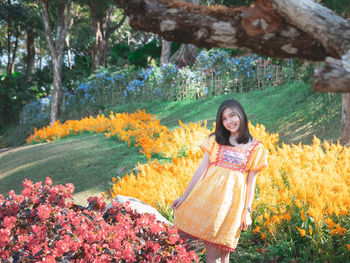 Portrait of a smiling young woman standing by flower plants