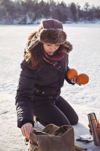 Woman holding oranges while kneeling on snow covered field