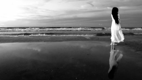 Rear view of woman standing with reflection on shore