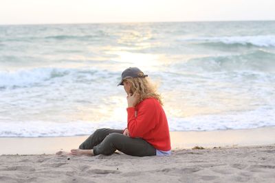 Blonde woman sitting on the ocean shore line during sunrise. alone concept, peace of mind, sadness