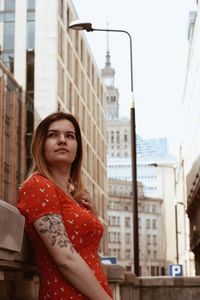 Side view of thoughtful beautiful woman standing against buildings in city