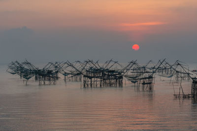 Fishing net in sea against sky during sunset