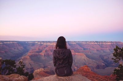 Rear view of woman sitting on cliff against grand canyon during sunset