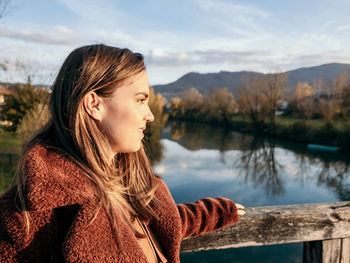 Portrait of young woman in winter coat on bridge over river.