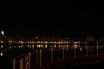 Illuminated bridge over river by buildings against sky at night