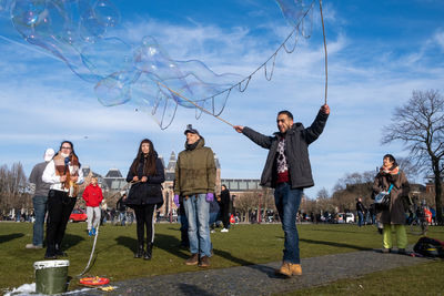 People playing with bubbles in park against sky