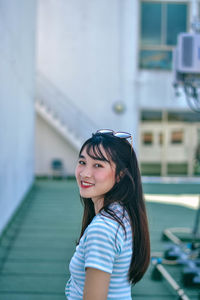 Portrait of smiling young woman standing on floor against building