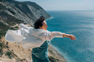 Adult woman with outstretched arms, like wings, on of a mountain against the backdrop of the sea