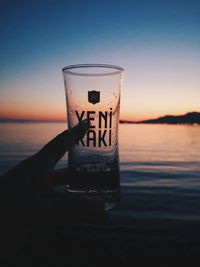 Beer glass on sea against sky during sunset