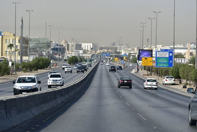 Traffic on road by buildings in city against sky