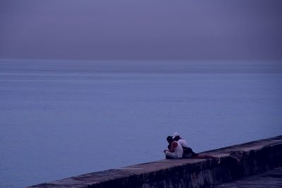 People sitting on retaining wall by sea