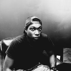 Portrait of serious young man sitting on chair against wall