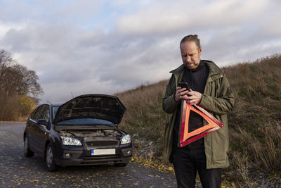 Man using cell phone while holding warning triangle