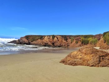 Rocks on beach against clear blue sky