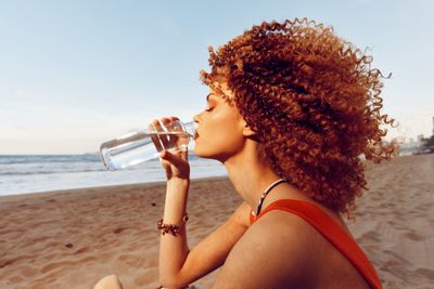 Young woman drinking water at beach