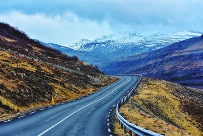 Empty road leading towards mountains against sky