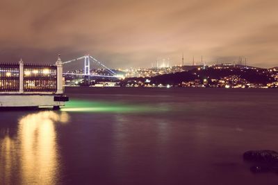 Illuminated bridge over river with city in background