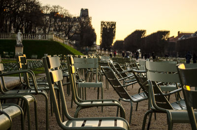 Empty chairs and tables in row against sky during sunset