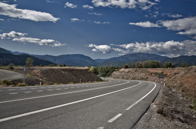 Empty road leading towards mountains against sky