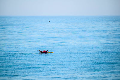 Man rowing boat in sea against clear sky