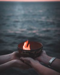 Cropped hands holding bowl with fire by sea