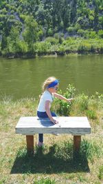 Side view of woman sitting by lake against trees