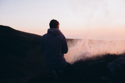 Rear view of man kneeling on mountain during sunset