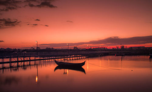 Silhouette boat moored on lake against orange sky