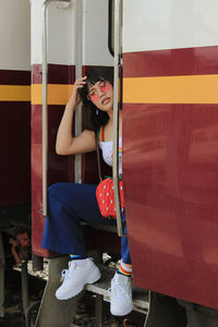 Portrait of young woman wearing sunglasses sitting at train entrance