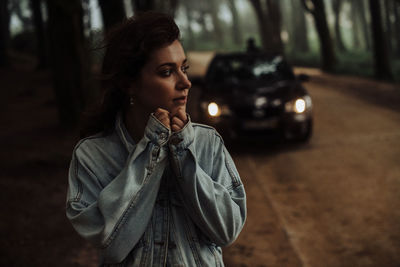 Close up of young woman standing alone in forest with car behind