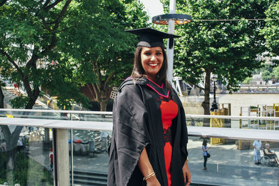 Portrait of smiling young woman wearing mortarboard against trees