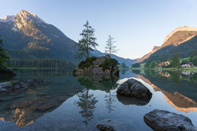 Crystal clear alpine tarn with rocky islands with tree on them during sunrise, hintersee, germany