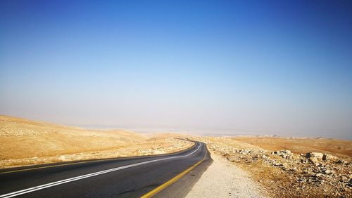 Road leading towards landscape against clear blue sky