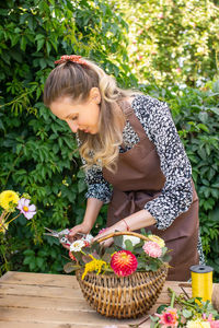 Cute florist girl collects a bouquet of autumn flowers in a basket on the table