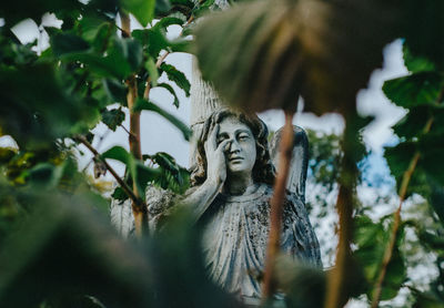 Old statue of aweeping stone angel on background of green leaves