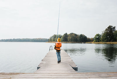 Man fishing on pier over lake against sky