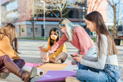 Females writing on posters while sitting on street