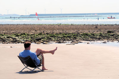 Rear view of man sitting on chair at beach