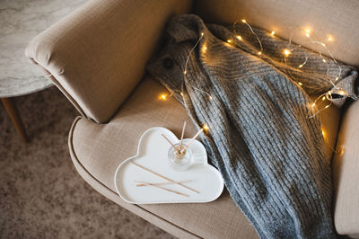 Knitted sweater and liquid home fragrance in glass bottle on tray in armchair top view.  