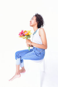 Young woman sitting on flower against white background