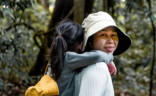 Portrait of smiling mother carrying daughter on back in forest