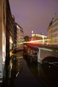 Illuminated bridge over river by buildings against sky at night