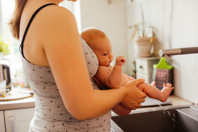 Midsection of mother holding urinating baby at kitchen sink