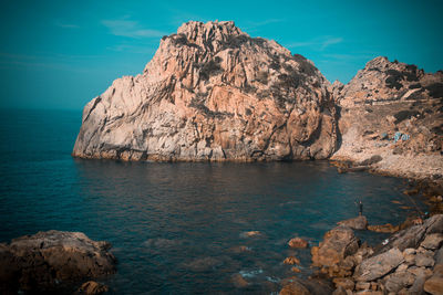 Rock formations by sea against blue sky