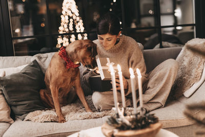 Happy woman with dog cuddling and unpacking gifts, looking excitedly into the box