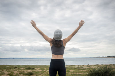 Rear view of a sporty woman with her arms raised in celebration by the sea, breathing fresh air.