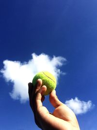 Cropped hand holding tennis ball against blue sky